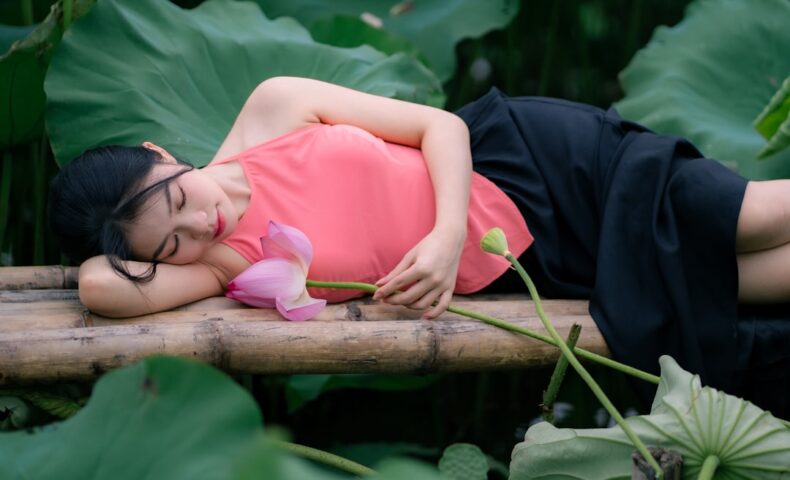 A woman sleeps among lotus leaves and flowers.
