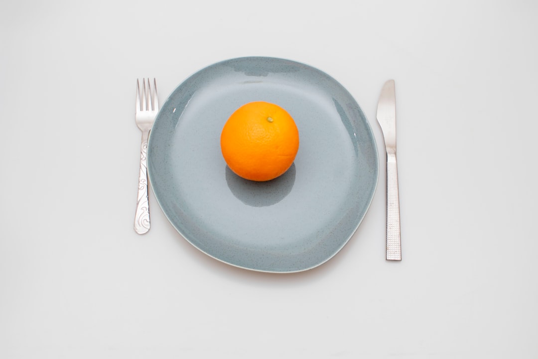 An orange sitting on a plate next to a fork and knife