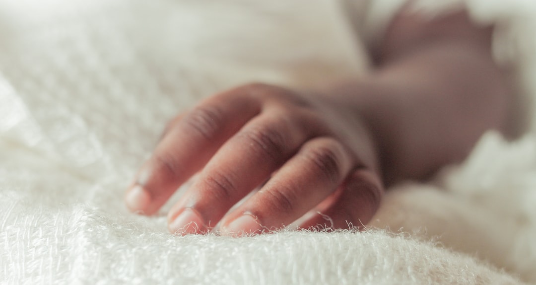 A baby's tiny hand rests on a blanket.