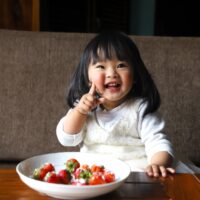 a little girl sitting in front of a bowl of fruit