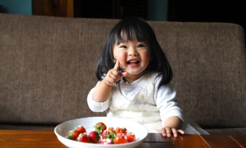 a little girl sitting in front of a bowl of fruit