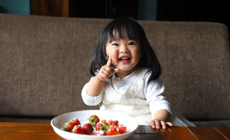a little girl sitting in front of a bowl of fruit