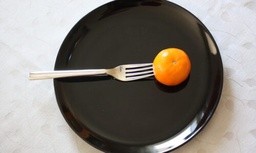 a black plate with a fork and an orange on it