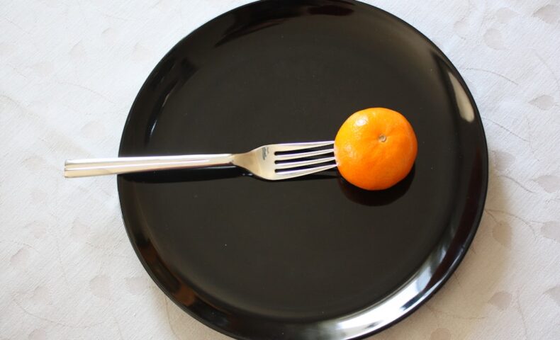 a black plate with a fork and an orange on it