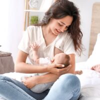授乳中の赤ちゃんを笑顔で抱く母親がベッドの上で母乳を与えている様子