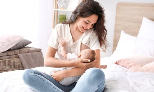 授乳中の赤ちゃんを笑顔で抱く母親がベッドの上で母乳を与えている様子