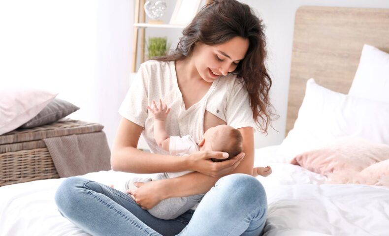 授乳中の赤ちゃんを笑顔で抱く母親がベッドの上で母乳を与えている様子