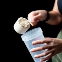 授乳中の女性がプロテインをシェイカーに入れている様子。産後の栄養補給に適したプロテインの選び方を表現した画像。