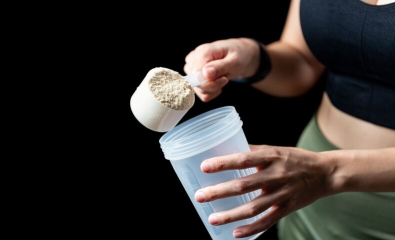 授乳中の女性がプロテインをシェイカーに入れている様子。産後の栄養補給に適したプロテインの選び方を表現した画像。