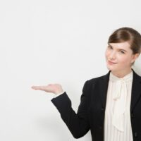 スーツ姿の女性が手のひらを見せながらプレゼンテーションをする様子