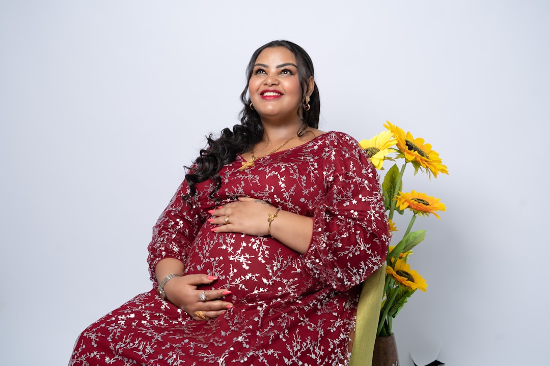 A pregnant woman sitting on a chair next to a vase of flowers