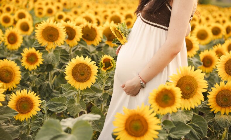 Pregnant woman poses in a field of sunflowers.