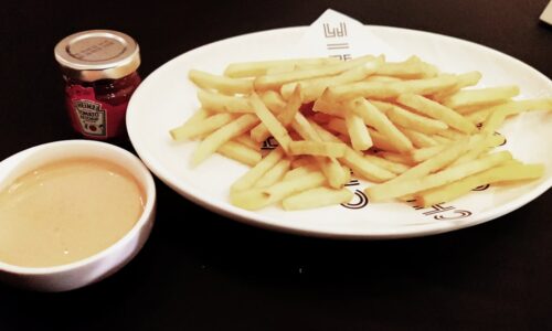 a white plate topped with french fries next to a cup of sauce